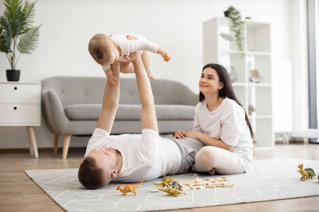 Vater hebt Baby hoch, während er mit der Mutter auf dem Boden liegt