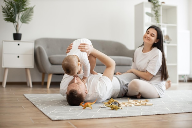 Vater hebt Baby hoch, während er mit der Mutter auf dem Boden liegt