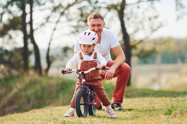 Vater im weißen Hemd bringt Tochter bei, wie man im Freien Fahrrad fährt