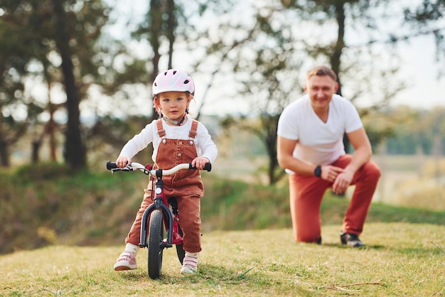 Vater im weißen Hemd bringt Tochter bei, wie man im Freien Fahrrad fährt