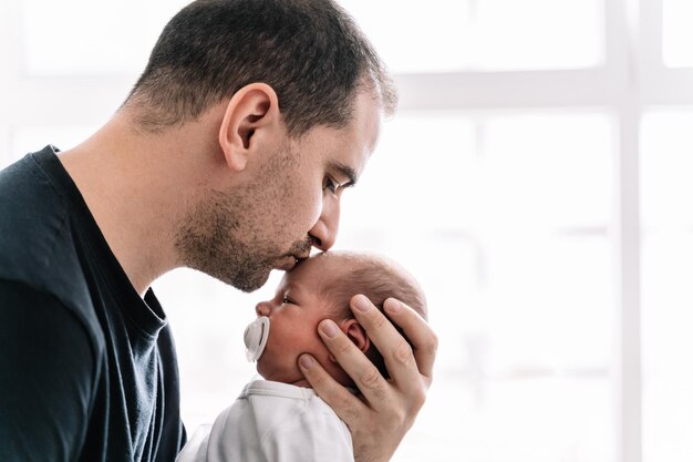 Vater küsst sein neugeborenes Baby auf die Stirn