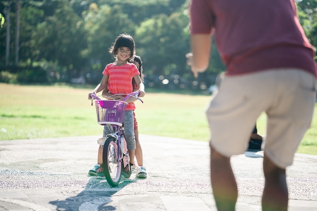 Vater lehrt Tochter im Park Fahrrad zu fahren
