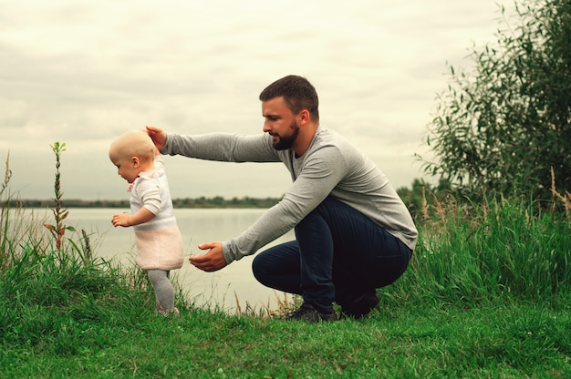 Vater lehrt Tochter in Park, Natur, Gras zu gehen. Vater und Tochter