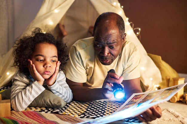 Vater liest seinem Sohn mit Taschenlampe ein Buch vor