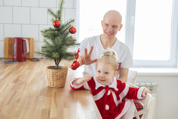 Vater mit Kleinkind-Tochter mit Cochlea-Implantaten, die Spaß an der Einbeziehung des Weihnachtswohnzimmers haben und innovative Behandlung für Taubheit mit Cochlea-Implantat-Chirurgie erfinden