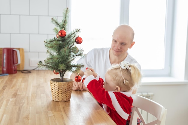 Vater mit Kleinkind-Tochter mit Cochlea-Implantaten, die Spaß an der Einbeziehung des Weihnachtswohnzimmers haben und innovative Behandlung für Taubheit mit Cochlea-Implantat-Chirurgie erfinden