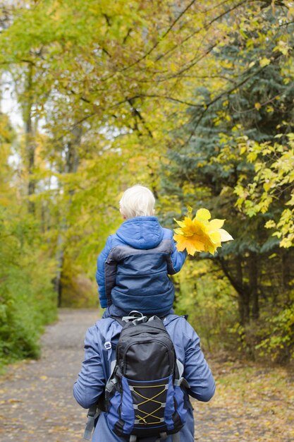 Foto vater mit seinem sohn auf den schultern im herbstwald spazieren. rückansicht