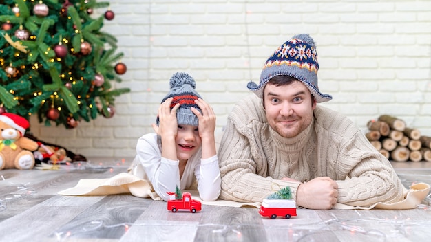 Vater mit seinem Sohn spielt zu Hause auf dem Boden in der Nähe des Weihnachtsbaumes. Glückliche Familienidee