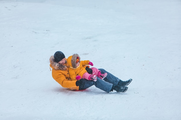 Vater mit Tochter in gelben Wintermänteln verschneiten Hügel gleiten
