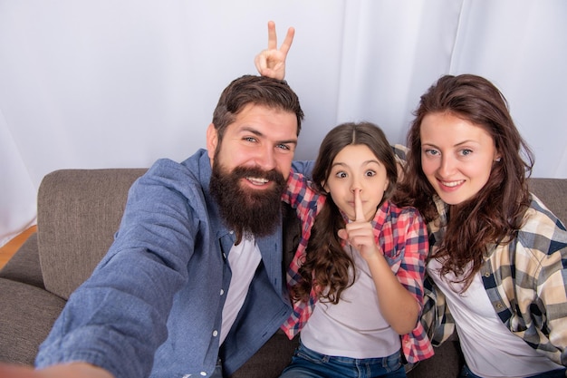 Vater, Mutter und Kind auf dem Sofa, freundliche Familie, die Spaß hat, positive, lustige Eltern mit Kind