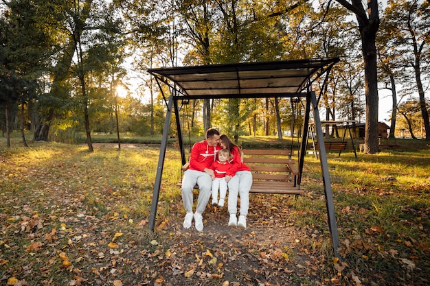 Vater, Mutter und kleine Tochter sitzen auf einer Holzschaukel im Herbstpark