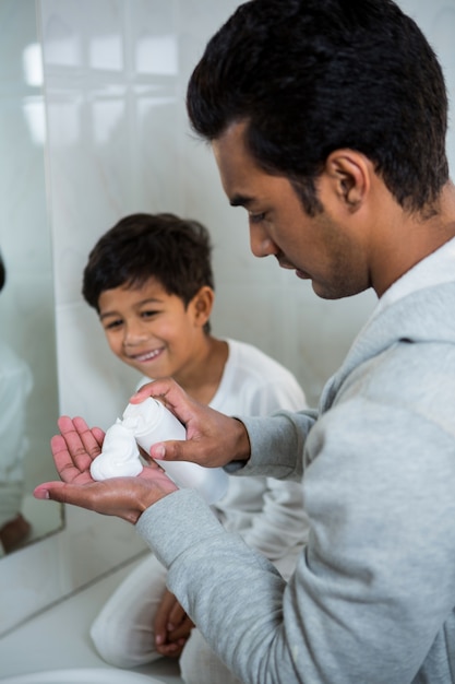 Vater sprüht Rasierschaum auf Hand, während Sohn schaut