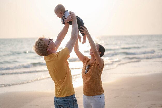 Vater trägt und spielt mit Kleinkind-Baby-Sohn und Mutter, die Spaß am Strand bei Sonnenuntergang im Urlaub haben. Familie, Strand, Entspannung, Sohn, Baby, Lifestyle-Konzept.