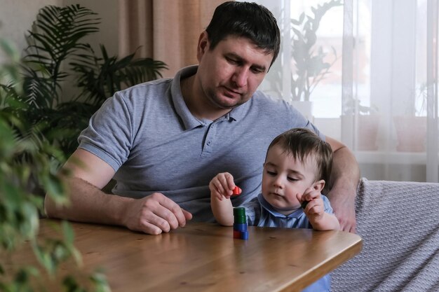 Vater und 1-jähriger Sohn spielen zu Hause mit Holzfiguren Entwicklung der Feinmotorik