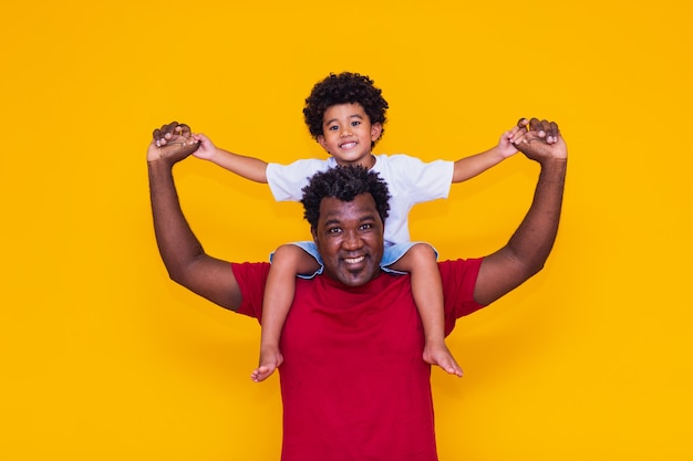 Vater und Afro-Sohn auf gelbem Hintergrund lächeln und spielen. Konzept zum Vatertag