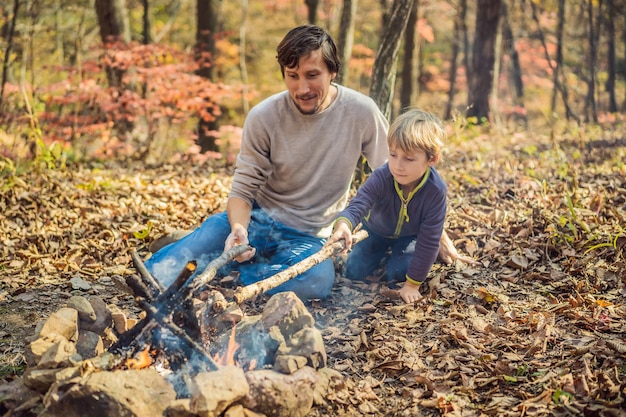 Vater und aufgeregter Sohn sitzen im Zelt im Wald beim Zelten mit Lagerfeuer