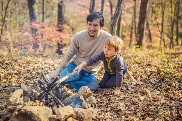 Vater und aufgeregter Sohn sitzen im Zelt im Wald beim Zelten mit Lagerfeuer