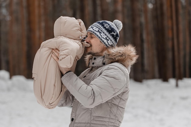 Vater und Baby gehen im Wald spazieren. Vater hält im Winter ein Baby im Arm. Vater und Tochter im Winter im Freien