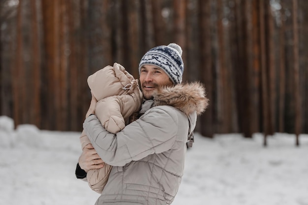 Vater und Baby gehen im Wald spazieren. Vater hält im Winter ein Baby im Arm. Vater und Tochter im Winter im Freien