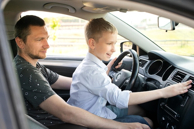 Vater und glücklicher Sohn auf dem Vordersitz eines Autos, das ein Auto fährt. Der Junge hält das Lenkrad