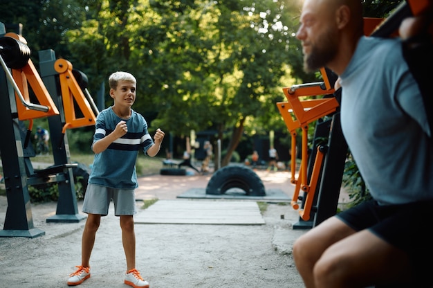 Vater und Junge am Trainingsgerät, Sporttraining auf dem Spielplatz im Freien. Die Familie führt einen gesunden Lebensstil, Fitnesstraining im Sommerpark