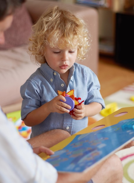 Vater und Junge lesen ein Buch über Bildung und Entwicklung und verbringen schöne Zeit zu Hause. Familie lehrt und lernt mit Mann und Kind und verbindet Bildergeschichten mit Spielzeugen für Wachstum