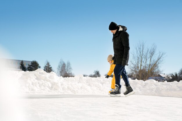 Vater und Kind halten zusammen Händchen beim Schlittschuhlaufen auf einer Eisbahn in der Natur im Freien