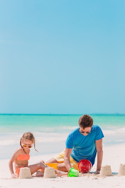 Vater und Kinder machen Sandburg am tropischen Strand. Familie spielt mit Strandspielzeug