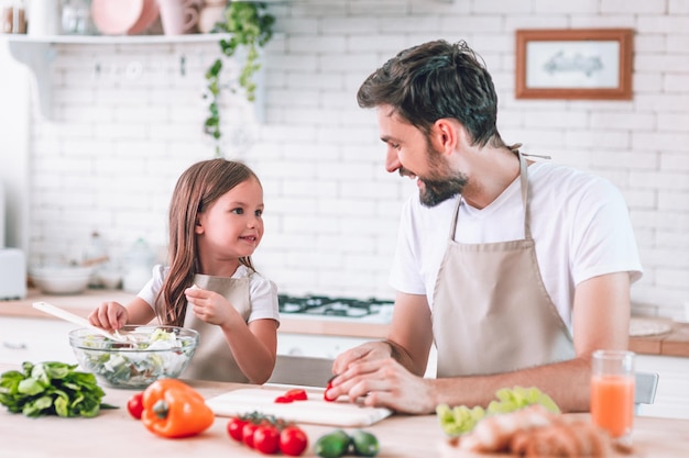 Vater und Mädchen bereiten gemeinsam Salat in der Küche zu und sehen sich an