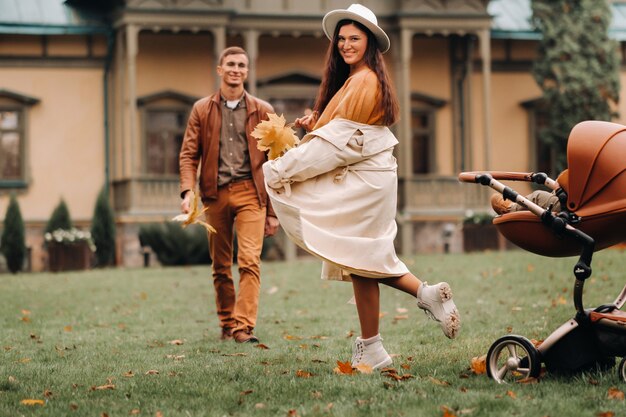 Vater und Mutter auf einem Spaziergang mit einem Kind in einem Kinderwagen im Herbstpark auf dem Landgut.