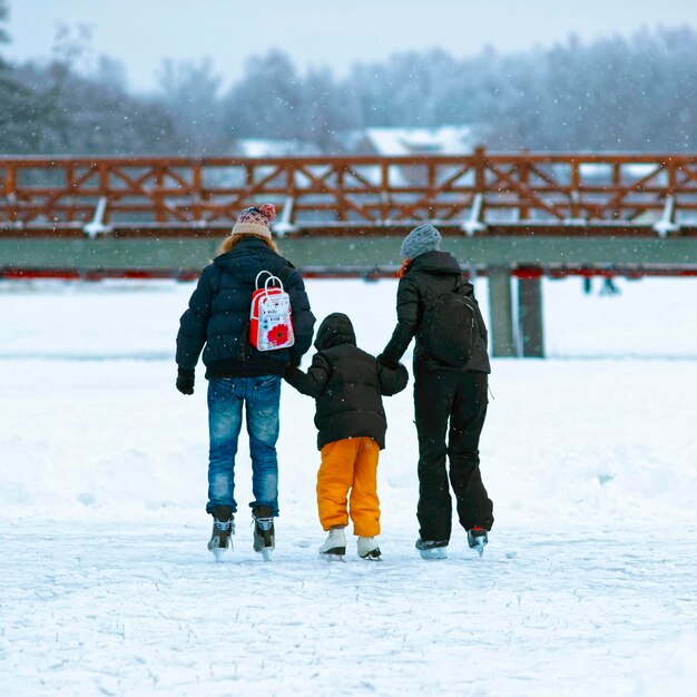 Vater und Mutter bringen Kindern im Winter das Skaten auf der Eisbahn bei. Skaten umfasst jede Sport- oder Freizeitaktivität, die darin besteht, mit Schlittschuhen auf Oberflächen oder auf Eis zu fahren.