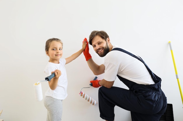 Vater und seine süße Tochter stehen und malen die Wand mit weißer Farbe und geben High Five