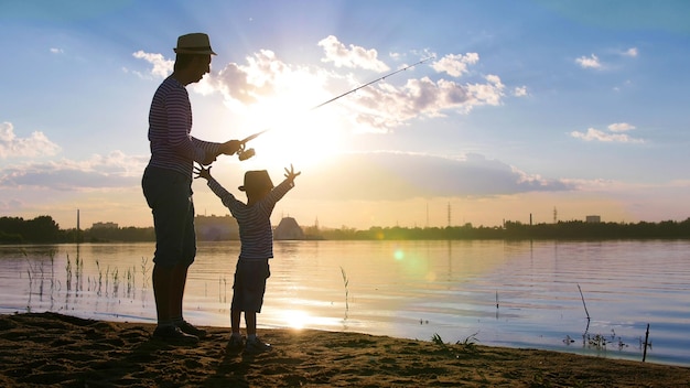 Vater und Sohn angeln am Flussufer in den Strahlen des Sonnenuntergangs
