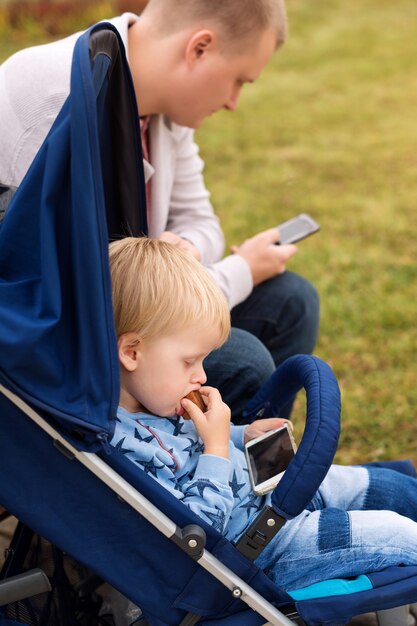 Vater und Sohn benutzen Smartphones, während sie Zeit miteinander im Herbstpark verbringen.