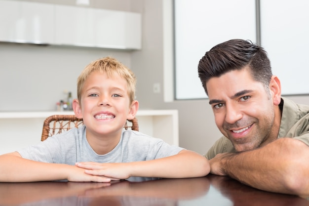 Vater und Sohn, die an der Kamera am Tisch lächeln