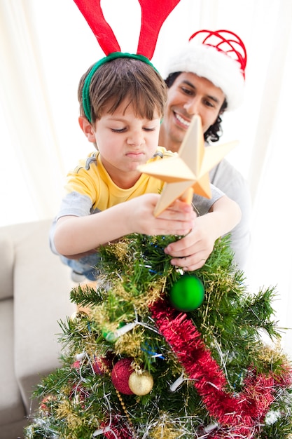 Vater und Sohn, die einen Stern auf die Oberseite eines Weihnachtsbaums setzen
