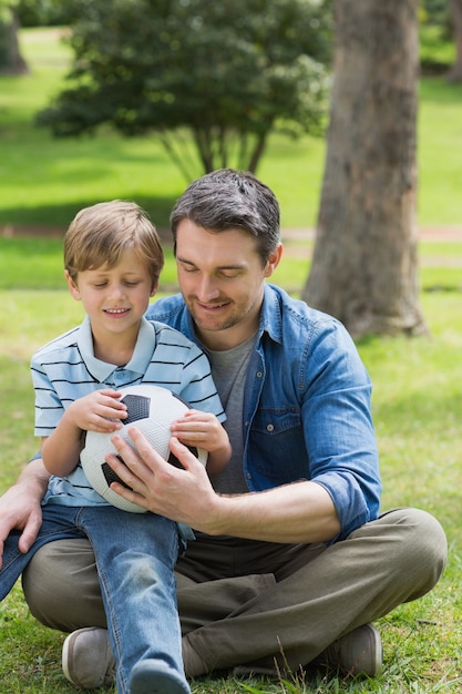 Vater und Sohn, die mit Ball am Park sitzen