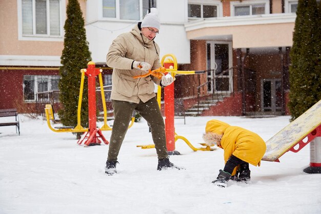 Vater und Sohn, die zusammen Spaß mit der Familie haben Winterferien Glückliches Kind, das Spaß im Schnee in der Stadt hat Winterspaß draußen