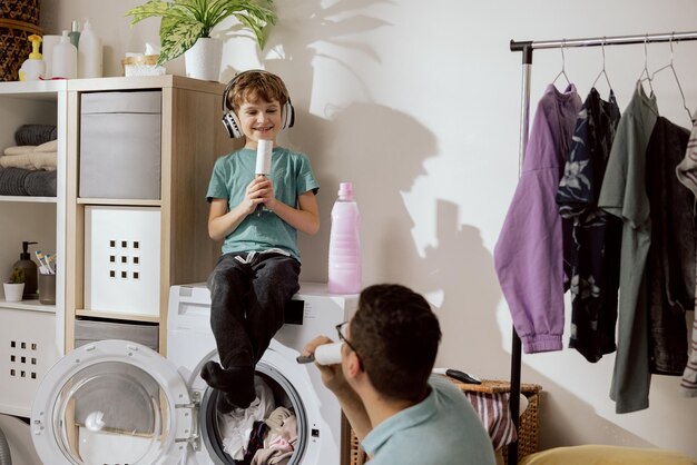 Vater und Sohn erledigen gemeinsam die Hausarbeit, Wäsche einlegen, der Junge sitzt zufrieden beim Waschen