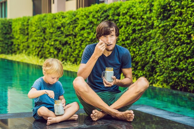 Vater und Sohn essen morgens Nachtisch mit Chiasamen und Mangos am Pool gesunde Ernährung