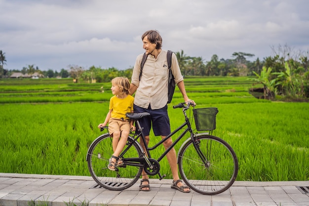 Vater und sohn fahren fahrrad auf einem reisfeld in ubud bali reise nach bali mit kinderkonzept