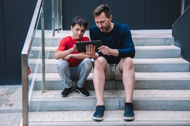 Vater und Sohn haben viel Spaß beim gemeinsamen Spielen auf dem Tablet. Moderne Technologien. Lebensstil. Foto in hoher Qualität