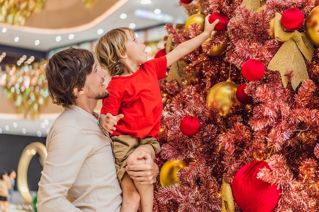 Vater und Sohn hängen eine Dekoration an den roten Weihnachtsbaum