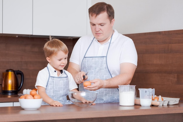 Vater und Sohn in der Küche Vater bringt Kind bei, Eier in eine Schüssel zu brechen Kochen