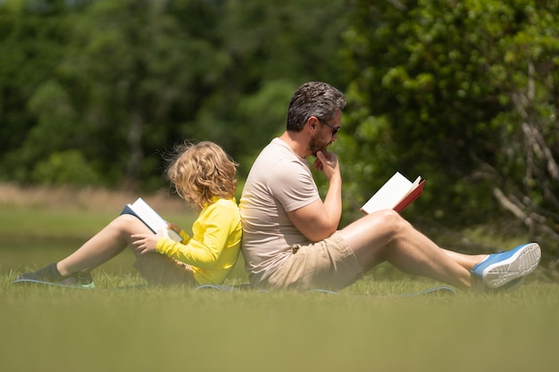 Vater und Sohn in der Schule im Freien lesen im Park ein Buch. Der Mann ermutigt den Jungen, sich mit der Familienerziehung vertraut zu machen