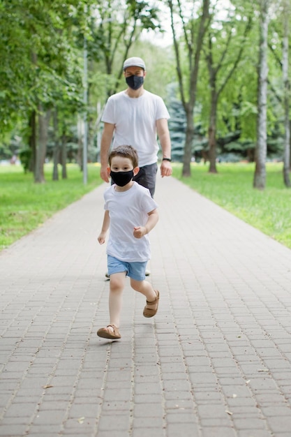 Vater und Sohn in schwarzen Gesichtsmasken gehen im Park spazieren Soziales Distanzierungs- und Quarantänekonzept