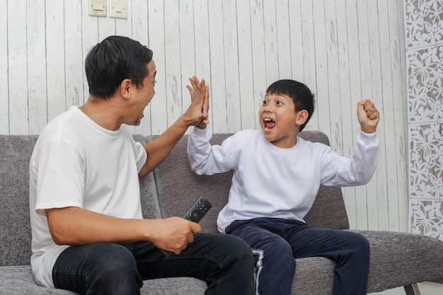 Vater und Sohn jubeln und machen High Five, während sie nach ihrem Lieblingsfußb fernsehen