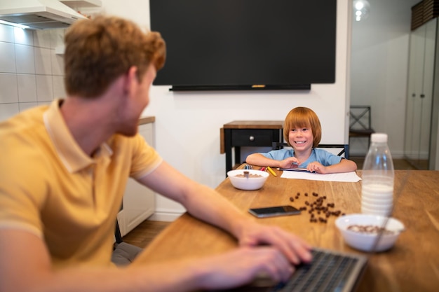 Vater und Sohn. Junger Mann, der am Laptop arbeitet, sein Kind sitzt neben ihm