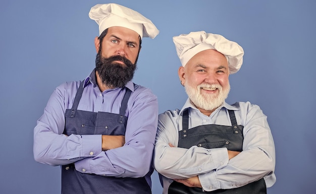 Vater und Sohn kulinarisches Hobby Reife bärtige Männer professionelle Restaurantköche Chefmänner tragen Schürzen Familienrestaurant Café-Arbeiter Restaurantküche Kulinarische Industrie Restaurantpersonal