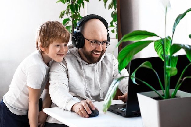 Vater und Sohn lachen, haben Spaß, spielen zu Hause Videospiele auf dem Laptop und verbringen Zeit miteinander